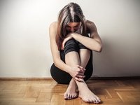 Traurige, ängstliche junge Frau kauert am Boden