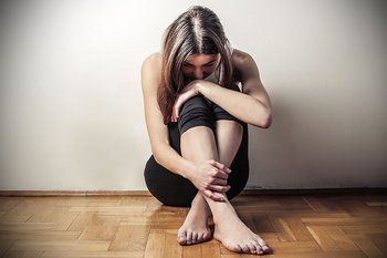 Traurige, ängstliche junge Frau kauert am Boden