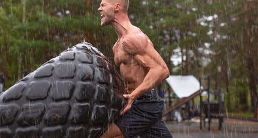 Schreiender Sportler wendet im Regen einen Traktorreifen