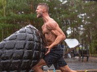 Schreiender Sportler wendet im Regen einen Traktorreifen