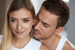 Junger Mann steht hinter seiner Partnerin und riecht an ihrem Hals