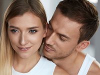 Junger Mann steht hinter seiner Partnerin und riecht an ihrem Hals