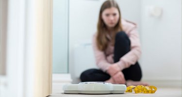 Waage, Maßband und im Hintergrund ein schüchternes Mädchen