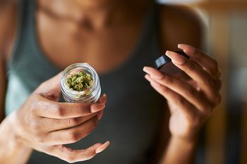 Junge Frau zeigt Glas mit medizinischem Cannabis