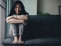 Einsame, traurige Frau kauert auf dem Sofa