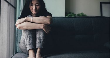 Einsame, traurige Frau kauert auf dem Sofa
