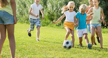Sechs Kinder spielen Fußball auf einer Wiese