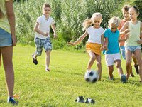 Sechs Kinder spielen Fußball auf einer Wiese