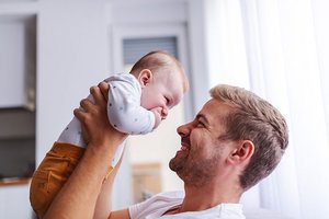 Junger Vater hebt Baby hoch, beide lächeln sich an